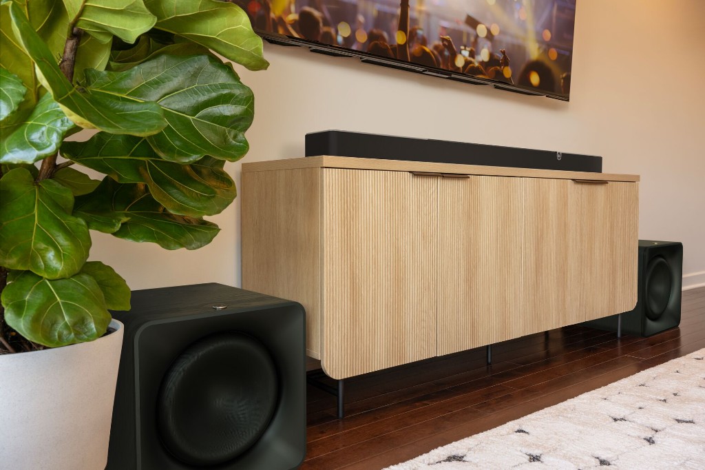 Klipsch Flexus wireless sound system in a modern living room — soundbar on a wood credenza with subwoofers